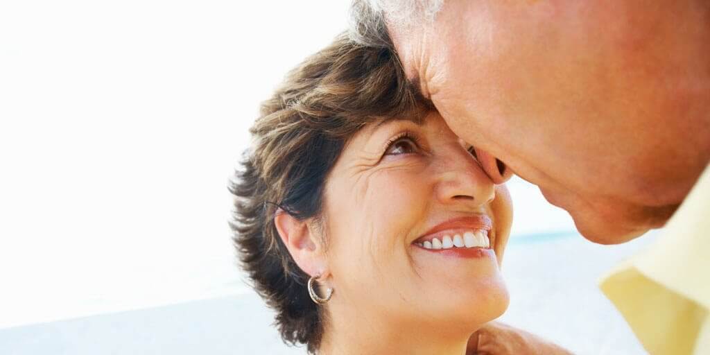 cataracts-at-a-glance A middle-aged couple is smiling and looking at each other outdoors.