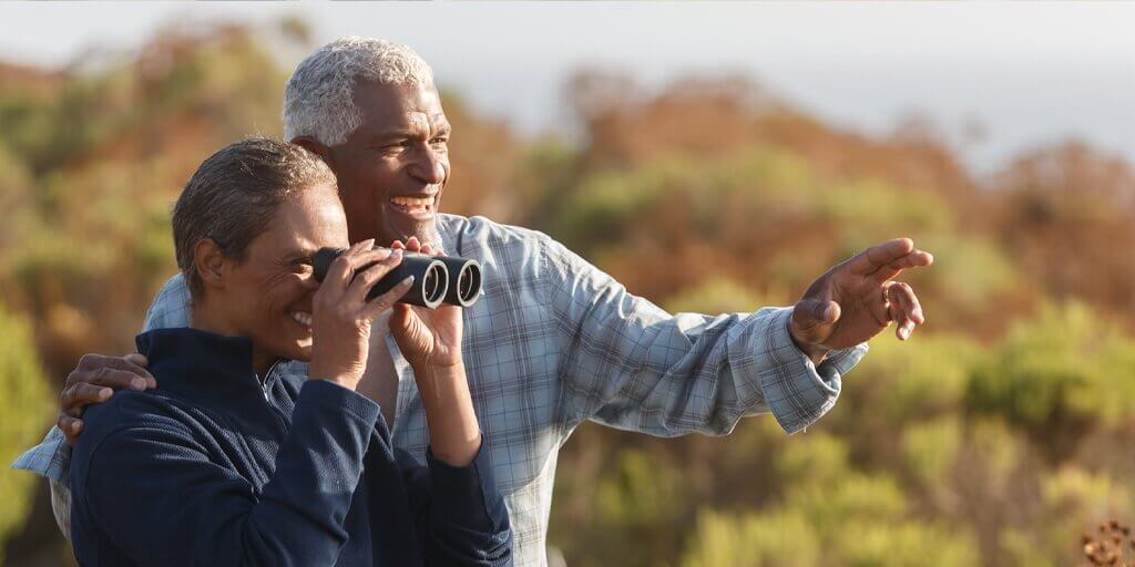 Senior couple outdoors with binoculars A senior couple outside pointing in the distance and looking through binoculars.
