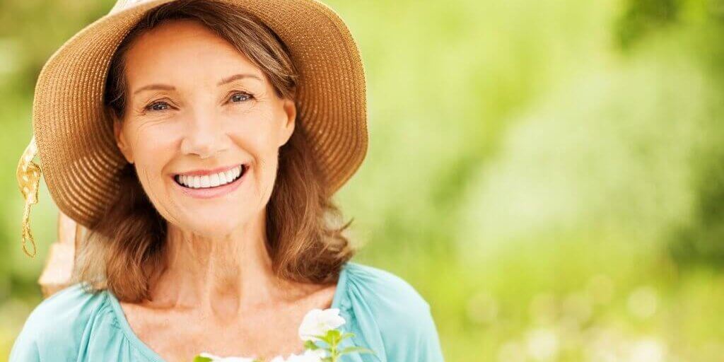 Happy Senior Woman Wearing Sun Hat With Flowers In Garden Middle-aged woman enjoying her day outdoors
