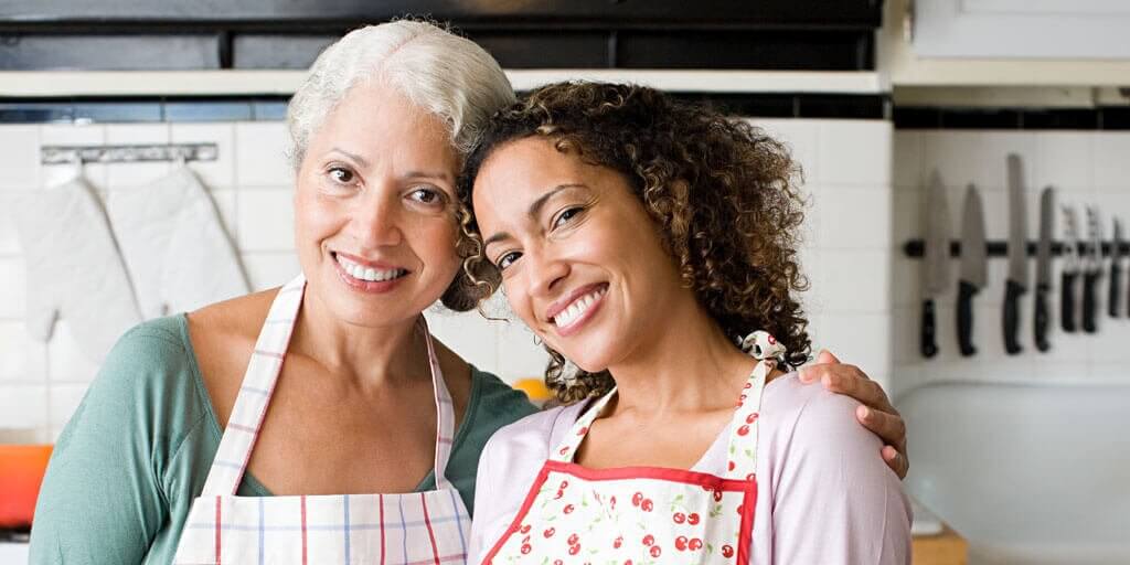 What-happens-to-our-eyes-1014x512 A senior mother and her daughter are smiling and standing in the kitchen together.